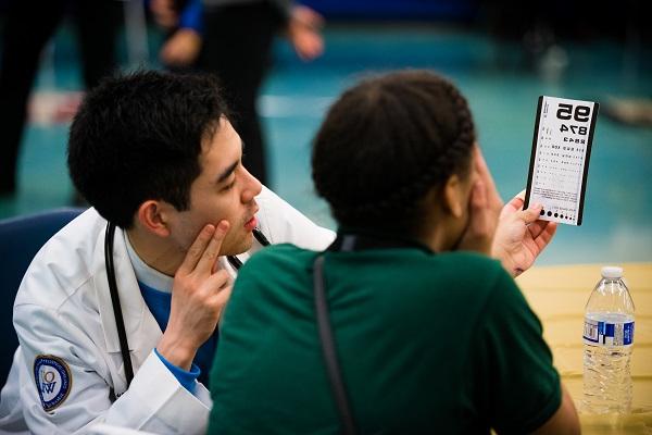 An OUWB student helps a student with an eye exam.